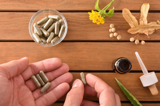 Hands taking natural medicine capsules on wooden table with plan - 写真・画像