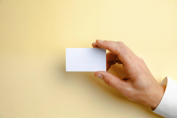 Male hand holding a blank business card on soft yellow background for text or design - Photo, Image