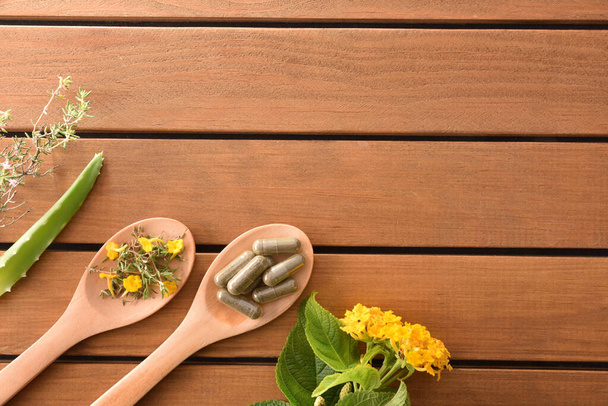 Cápsulas de medicina natural y plantas en madera cuchara superior
 - Foto, imagen