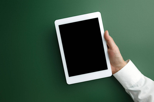 männliche Hand hält Tablet mit leerem Bildschirm auf grünem Hintergrund für Text oder Design - Foto, Bild