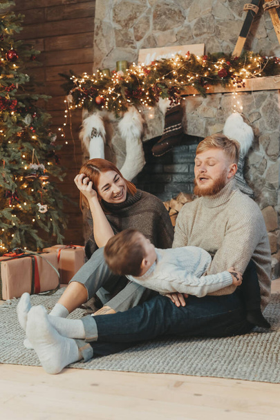 Young caucasian family mom dad son near fireplace christmas tree - Zdjęcie, obraz