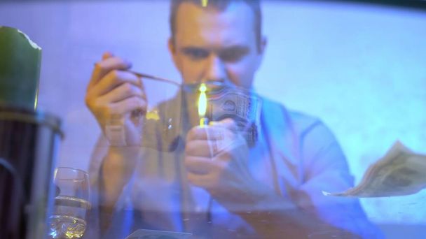 a man is preparing a drug in a spoon, holding it over the flame of a lighter. view through a glass countertop. - Foto, Bild