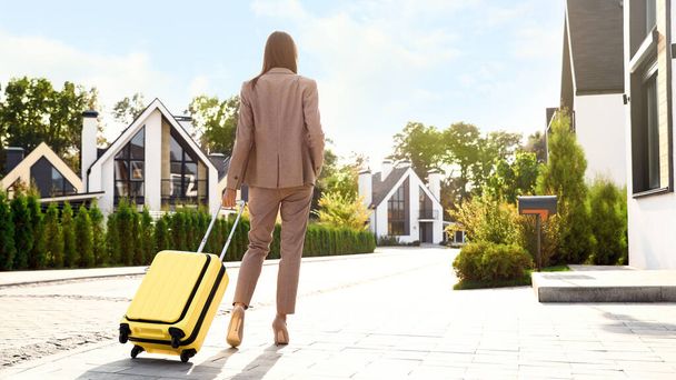 Young businesswoman with suitcase outdoors, back view. Moving day - Foto, Bild