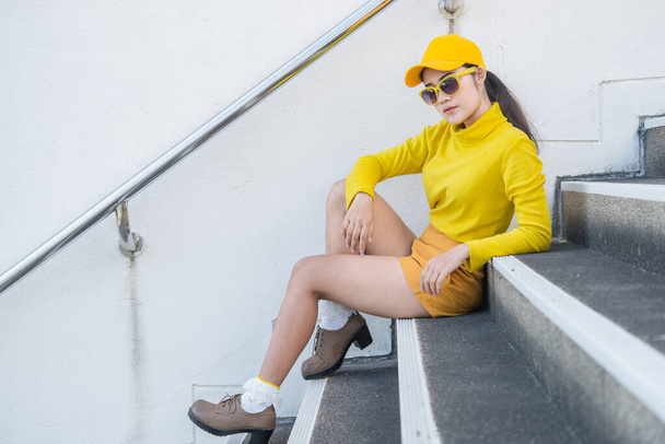 Portrait of beautiful asian woman in yellow cloths,Hipsters girl wear yellow hat on stair for take a picture,Thailand people in yellow tone style - Фото, изображение