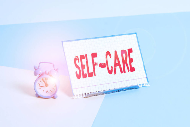 Word writing text Self Care. Business concept for practice of taking action to preserve or improve ones own health Mini size alarm clock beside a Paper sheet placed tilted on pastel backdrop. - Photo, Image