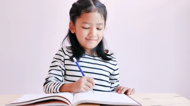 The little Asian girl wore a black and white striped dress. The kid used a pencil to draw on a notebook. - Footage, Video