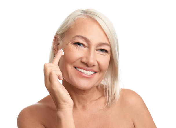 Mulher madura aplicando creme facial no fundo branco
 - Foto, Imagem