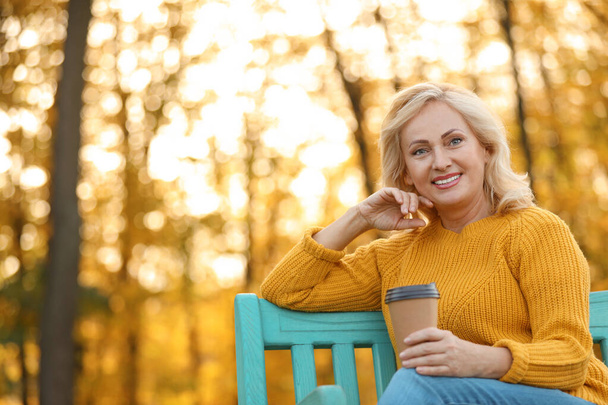 Beautiful mature woman with cup of coffee on bench in park - Φωτογραφία, εικόνα
