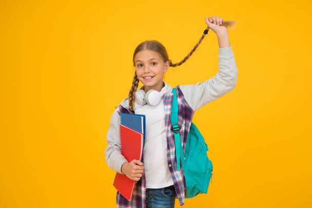 Long and braided. Cute small schoolchild hold long hair braid on yellow background. Adorable little girl wear long hair style. Styling long hair for school - Fotografie, Obrázek
