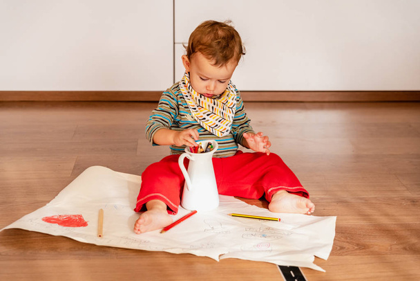 Bebé de 1 año en casa usando lápices de colores para pintar sobre papel
. - Foto, Imagen