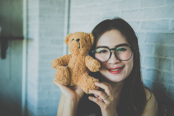 Beautiful asian woman wear glasses with teddy bear in coffee shop vintage style - Photo, image