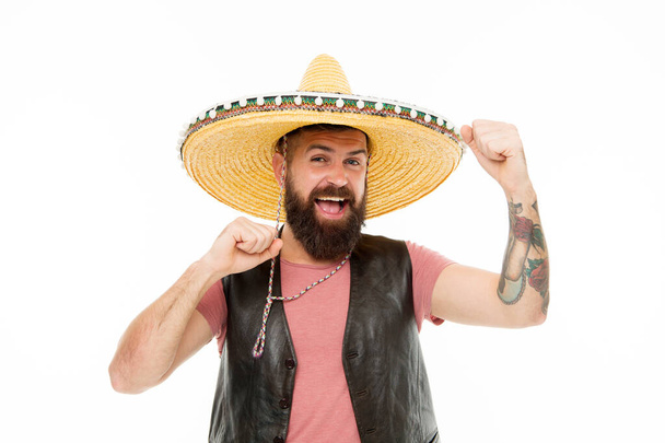 Adding hat to his spanish costume. Bearded man smiling in traditional sombrero hat. Happy hipster with beard and mustache wearing casual clothes and mexican hat. Mexican man in traditional straw hat - Valokuva, kuva