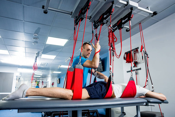 Physiotherapy. Suspension training therapy. Young man doing fitness traction therapy with suspension-based exercise training system - 写真・画像