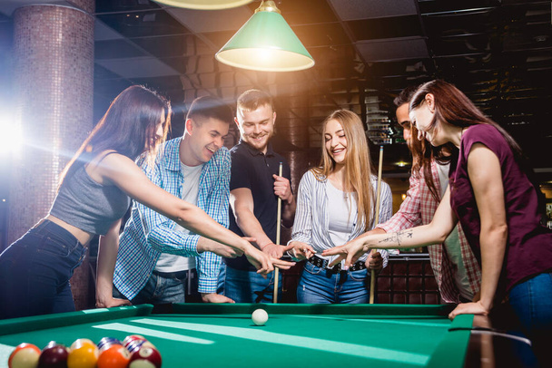 Group of young cheerful friends playing billiards. Funny time after work - 写真・画像