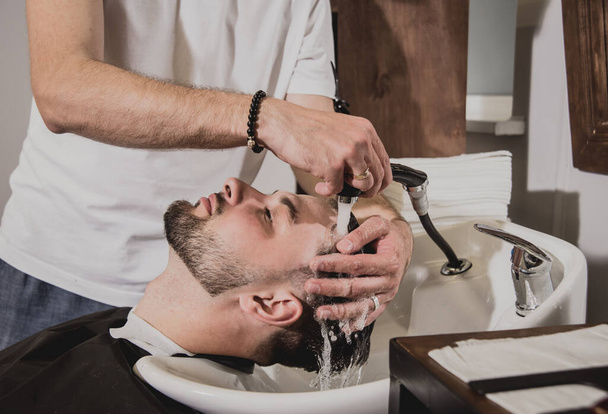 Young man with trendy haircut at barber shop. Barber washes customer head. Concept barbershop. - Photo, Image