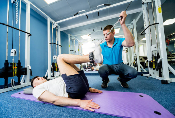 Rehabilitation therapy. Young man doing exercises on mat under supervision of physiotherapist. Treatment pain in spine - Фото, зображення