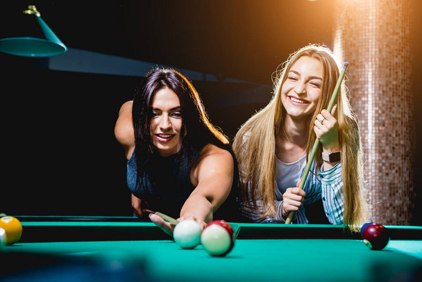 Two young women playing in billiard. Billiard room on the background. - Photo, Image