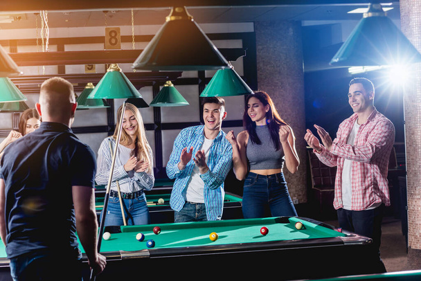 Group of young cheerful friends playing billiards. Funny time after work - Foto, Imagen