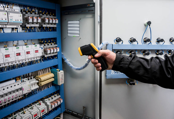close up of technician using infrared thermal imaging camera to check temperature at fuse-box - 写真・画像