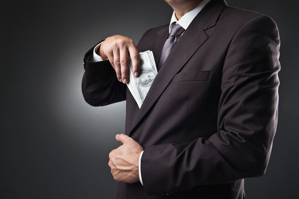 Businessman putting money in his pocket on dark - 写真・画像