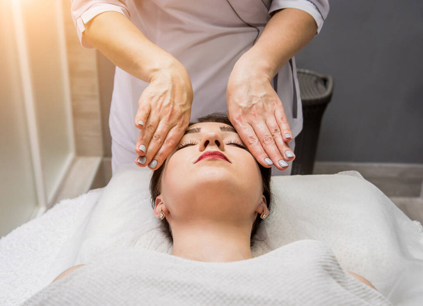 Beautiful young woman enjoying head massage in spa salon. Cosmetology concept - Zdjęcie, obraz