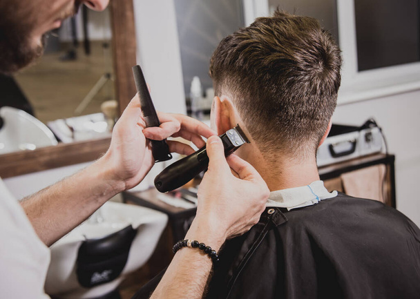 Young man with trendy haircut at barber shop. Barber does the hairstyle and beard trim. Concept barbershop. - Fotografie, Obrázek