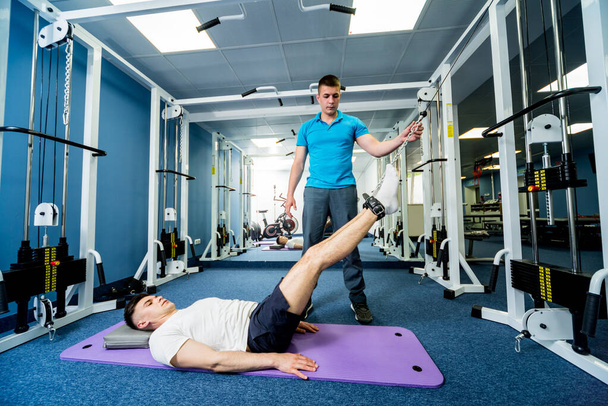 Rehabilitation therapy. Young man doing exercises on mat under supervision of physiotherapist. Treatment pain in spine - Foto, afbeelding