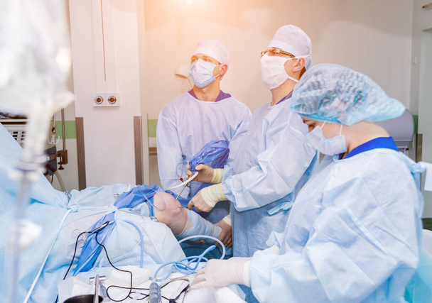 Arthroscope surgery. Orthopedic surgeons in teamwork in the operating room with modern arthroscopic tools. Knee surgery. Hospital background - 写真・画像