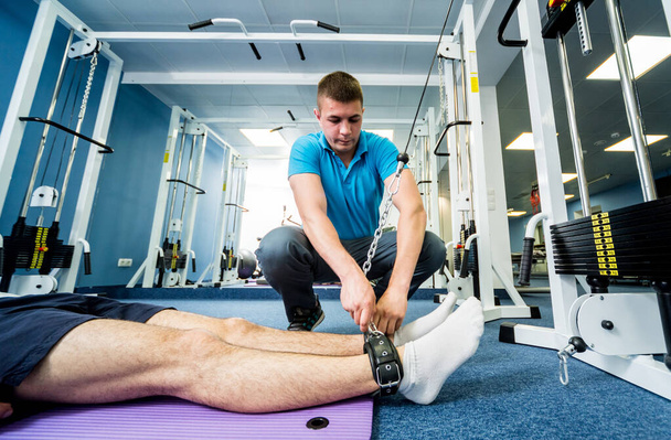 Rehabilitation therapy. Young man doing exercises on mat under supervision of physiotherapist. Treatment pain in spine - Fotografie, Obrázek