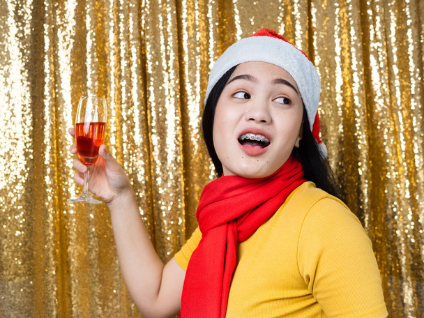 Happy Asian woman with red Santa hat and drinking red wine on go - Foto, Imagem