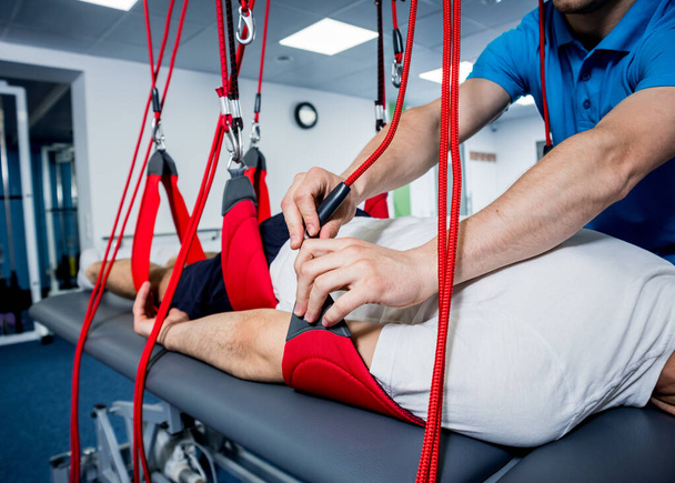 Physiotherapy. Suspension training therapy. Young man doing fitness traction therapy with suspension-based exercise training system. Treatment of pain in the spine. - Zdjęcie, obraz