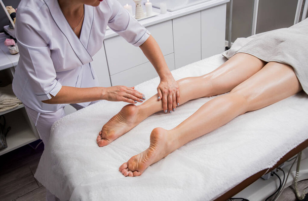 Beautiful young woman enjoying legs massage in spa salon. Cosmetology concept - Zdjęcie, obraz