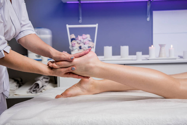 Beautiful young woman enjoying foot massage in spa salon. Cosmetology concept - 写真・画像