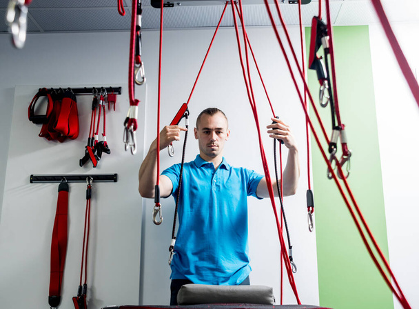 Suspension training therapy. Young man doing fitness traction therapy with suspension-based exercise training system. Treatment of pain in the spine. - Фото, зображення