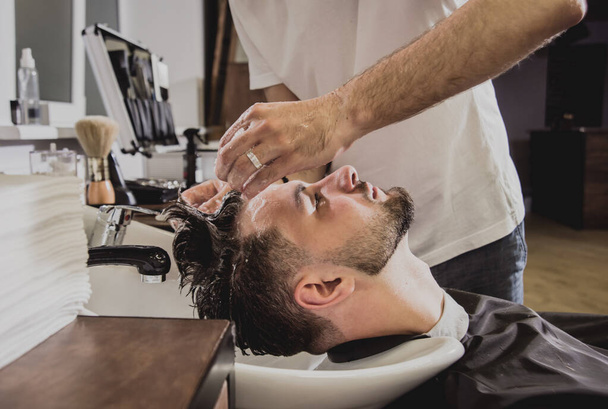 Fiatal férfi divatos frizurával a fodrászatban. A borbély mossa a vásárlók fejét. Koncepciófodrászat. - Fotó, kép