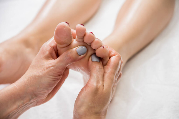 Beautiful young woman enjoying foot massage in spa salon. Cosmetology concept - Фото, изображение