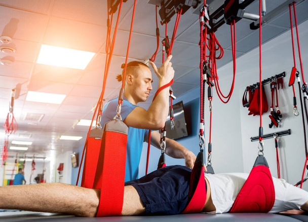 Physiotherapy. Suspension training therapy. Young man doing fitness traction therapy with suspension-based exercise training system - Foto, afbeelding