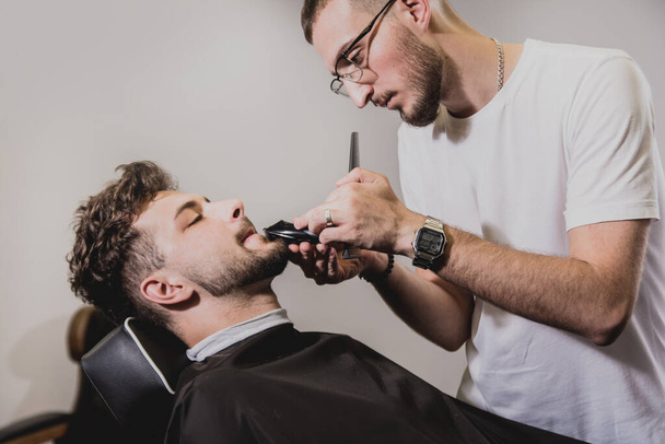 Young man with trendy haircut at barber shop. Barber does the hairstyle and beard trim. Concept barbershop. - Photo, image