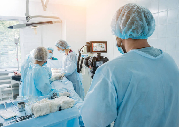 A videós sebészt és asszisztenseket lő le a műtőben sebészeti felszereléssel.. - Fotó, kép