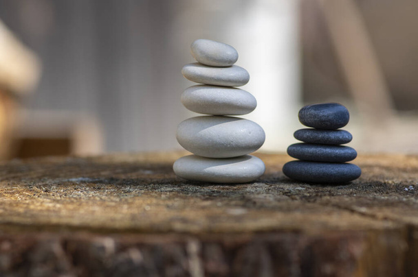White black stone cairns, poise light pebbles on wood stump in front of brown natural background, zen like, harmony and balance - Photo, Image