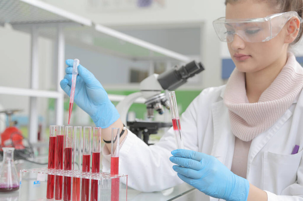 Laboratuvarda test tüpleriyle çalışan genç kadın laboratuvar bilim adamı. - Fotoğraf, Görsel