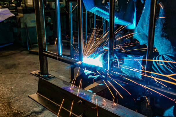 A welder at work in a workshop produces metal structures. Sparks from welding fly around. - Photo, Image