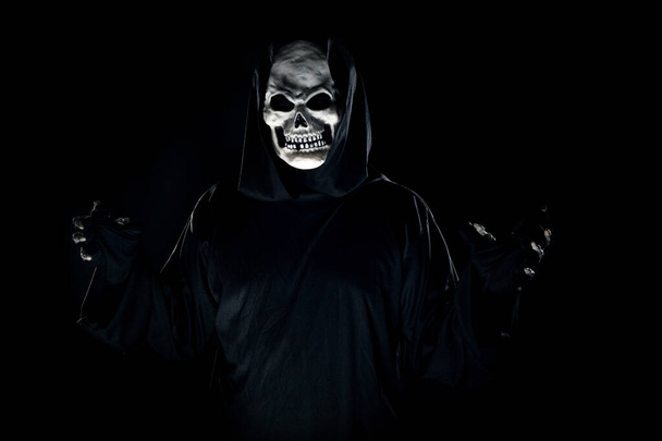 Scary monster or grim reaper ghost coming out of the dark shadows to haunt during Halloween.  Depicts a scary and deadly fictitious demon - Photo, image