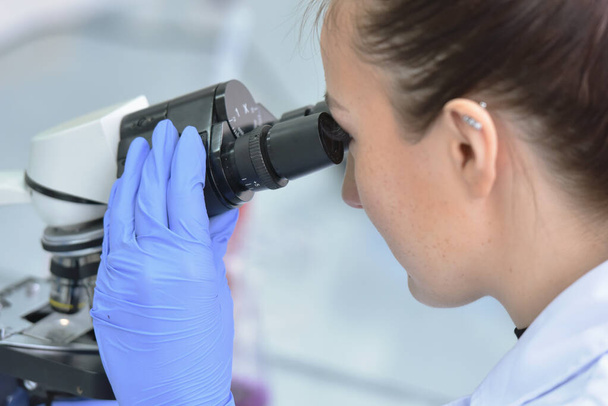 Jeune scientifique femelle regardant à travers un microscope dans une la - Photo, image