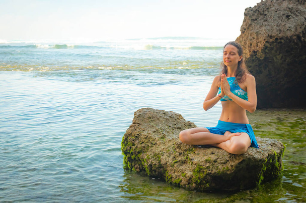 Молода жінка сидить на скелі, медитуючи, практикуючи йогу і пранаяму на пляжі Балі. Руки в іменистих мудрі - Фото, зображення