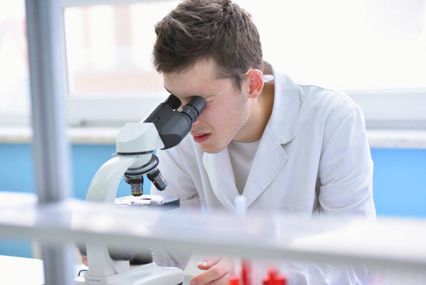 Jonge mannelijke wetenschapper kijkt door een microscoop in een laborator - Foto, afbeelding