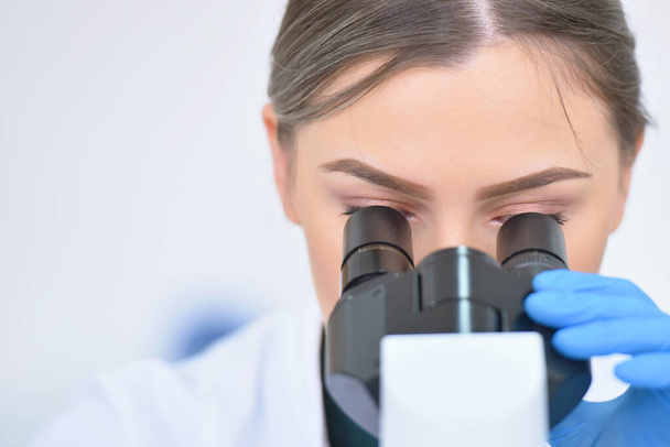 Young female male scientist looking through a microscope in a la - Foto, immagini