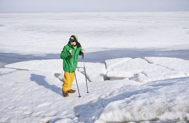Young adult man with walking sticks outdoors exploring icy lands - Fotó, kép