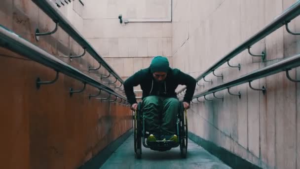 Niepełnosprawny mężczyzna na wózku inwalidzkim wstaje na długiej specjalnej rampie czasami opierając się o balustradę - Materiał filmowy, wideo