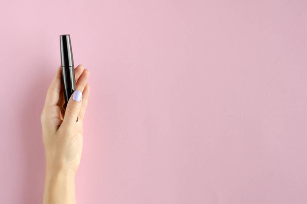 Hand with black mascara composition on pink background. - Foto, Imagem